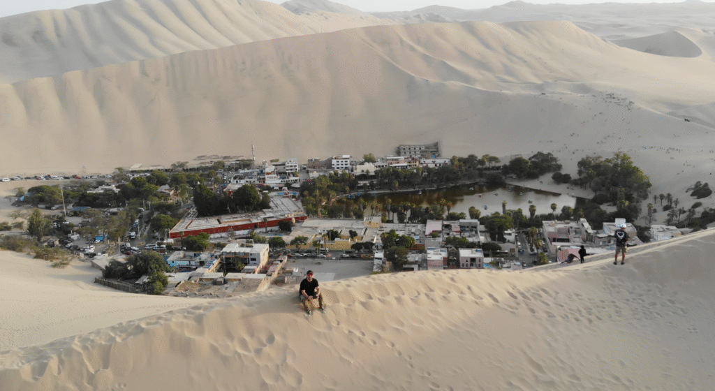 David C. Berruezo de pie en la cima de una gran duna de arena con vistas al oasis de Huacachina, Perú